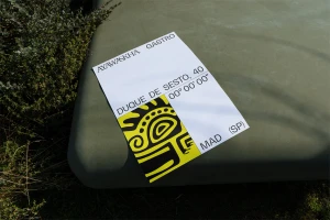 Printed card with Ayawaskha Gastro typography and tribal graphic resting on an olive green textured surface with foliage.