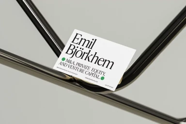 A white business card with serif typography rests on a reflective chrome and glass surface.