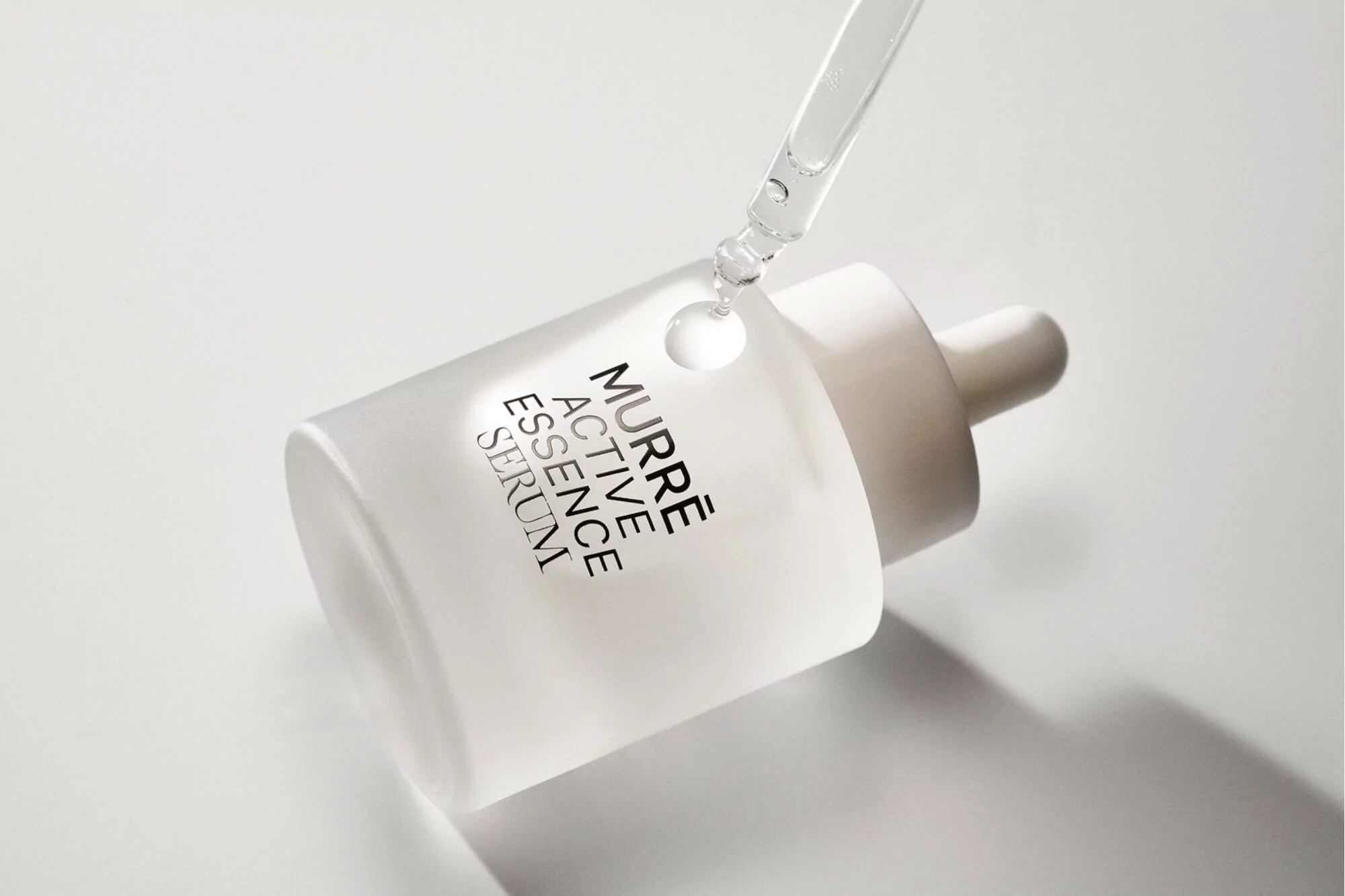 Serum bottle with dropper on white backdrop, featuring the text "MURRÈ ACTIVE ESSENCE SERUM" for skincare or cosmetic advertising.