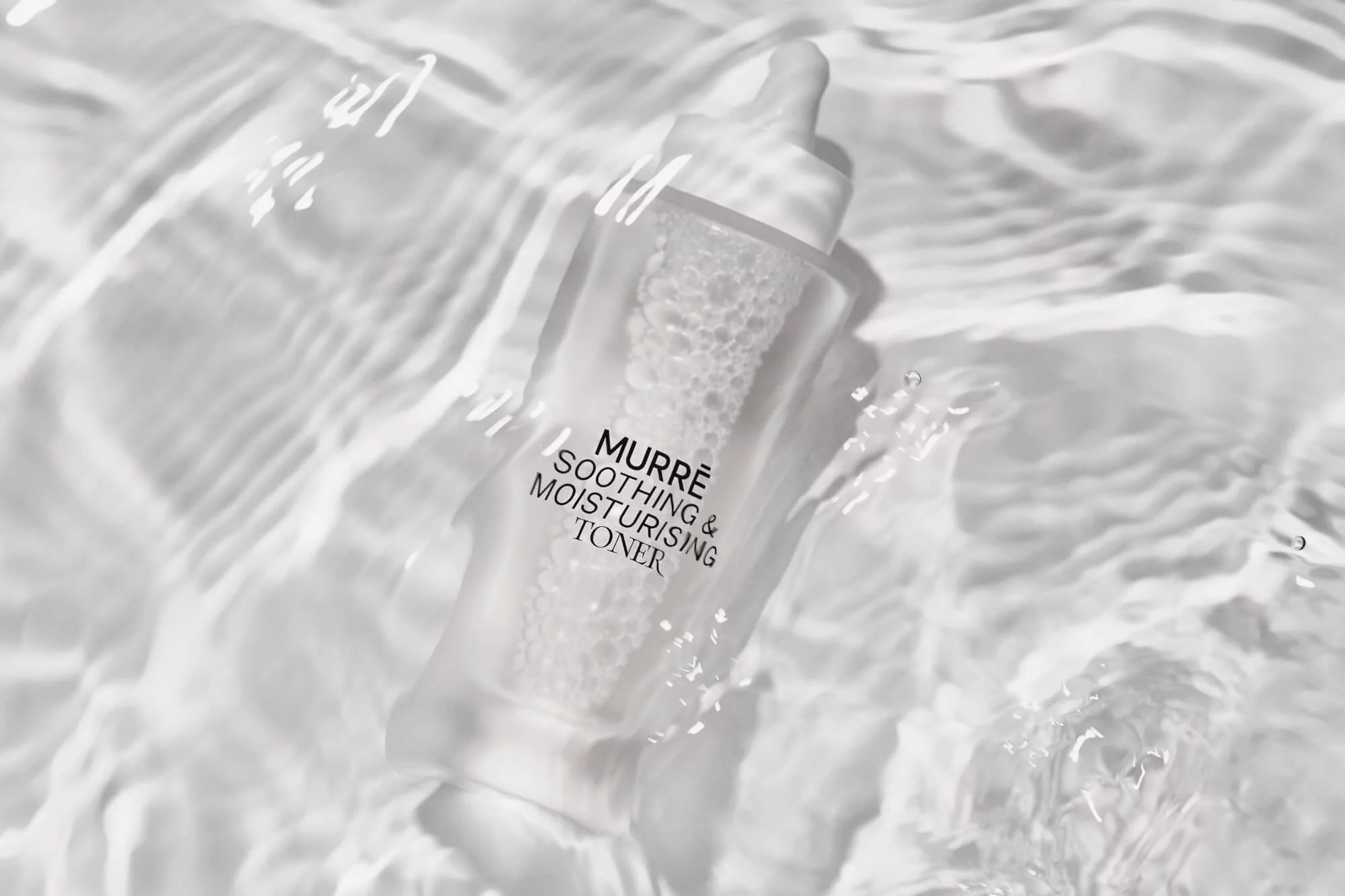 Clear bottle of Murre Soothing & Moisturising Toner sits submerged in clear water with light refracting on the surface of the water.