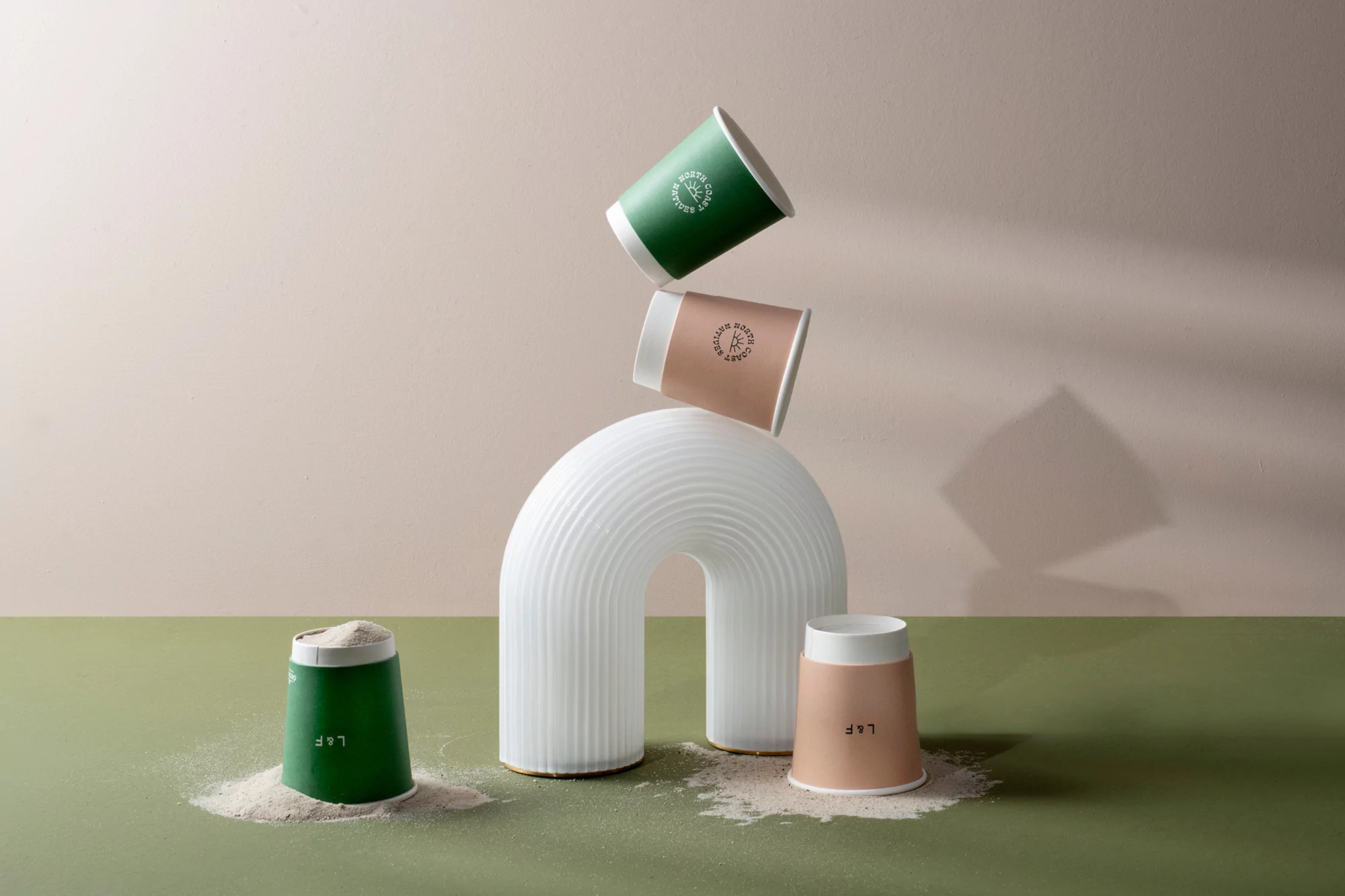 Studio shot featuring stacked green and peach cups around white arch on a green surface with pale beige backdrop, good for cafe design.