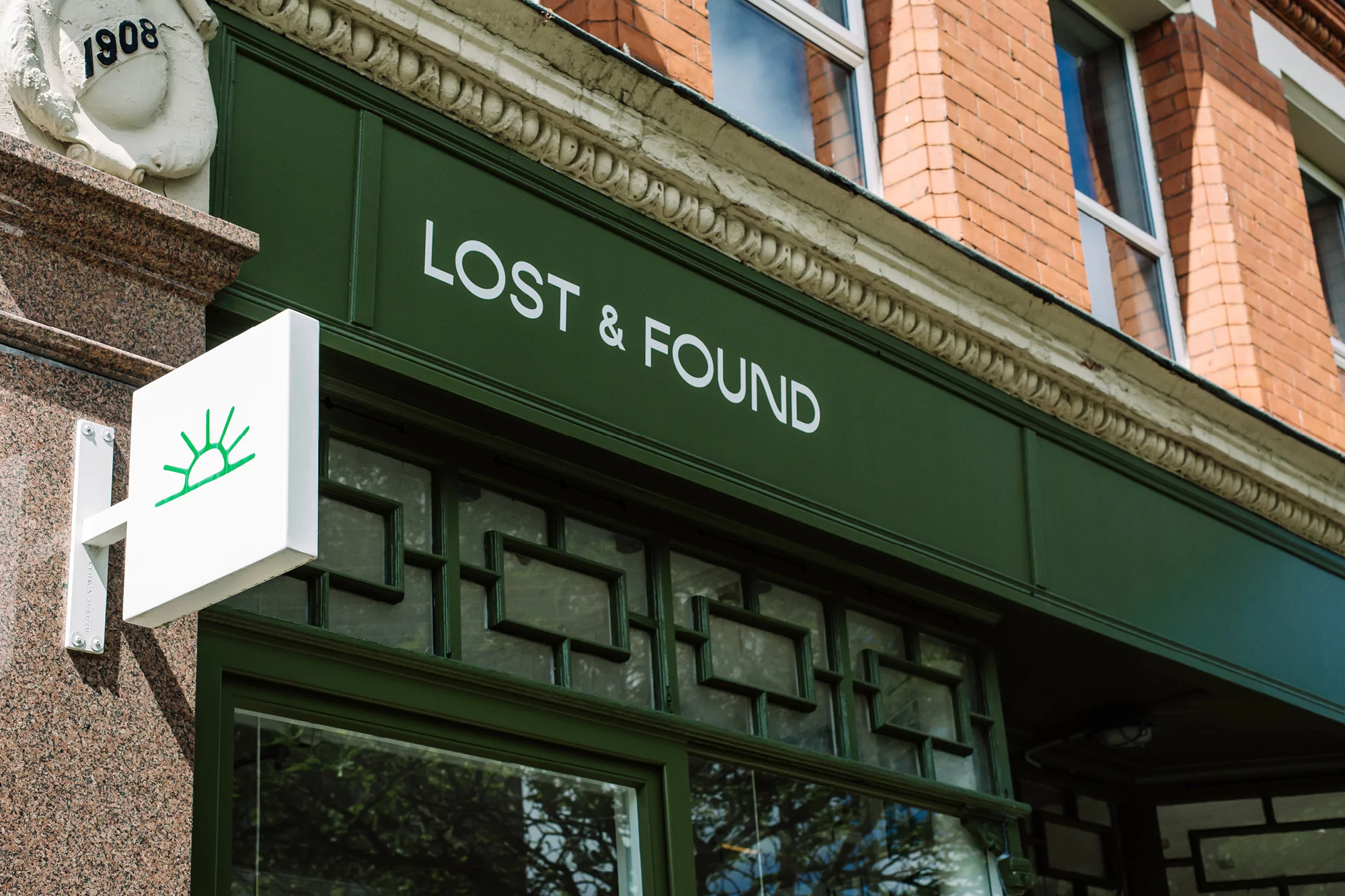 Exterior of a building featuring the 'Lost & Found' storefront with an illuminated sign, and a sun logo on a white square sign.