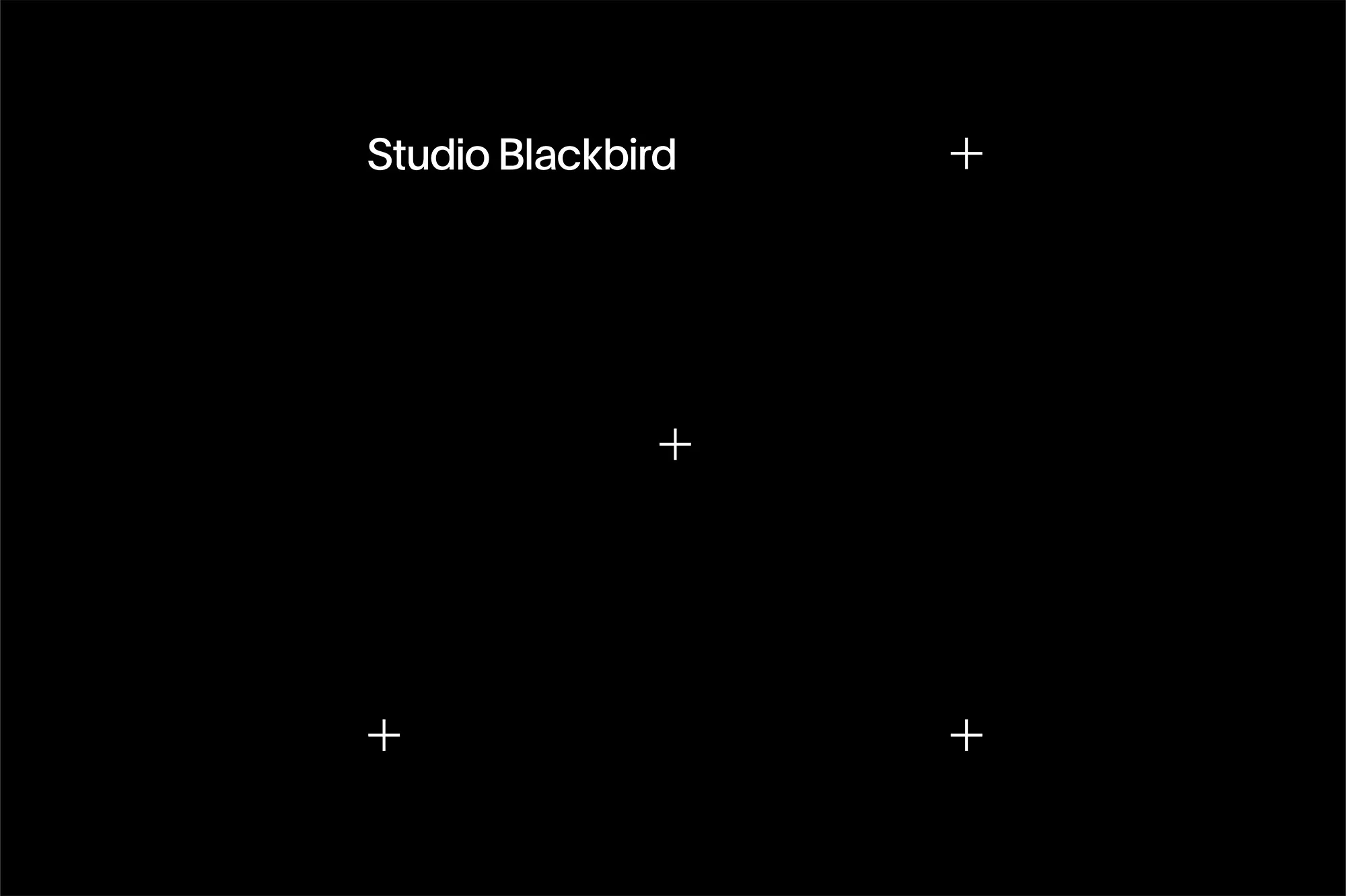 Minimalist black backdrop with white text 'Studio Blackbird' and simple plus sign alignment markers for studio photography and video.