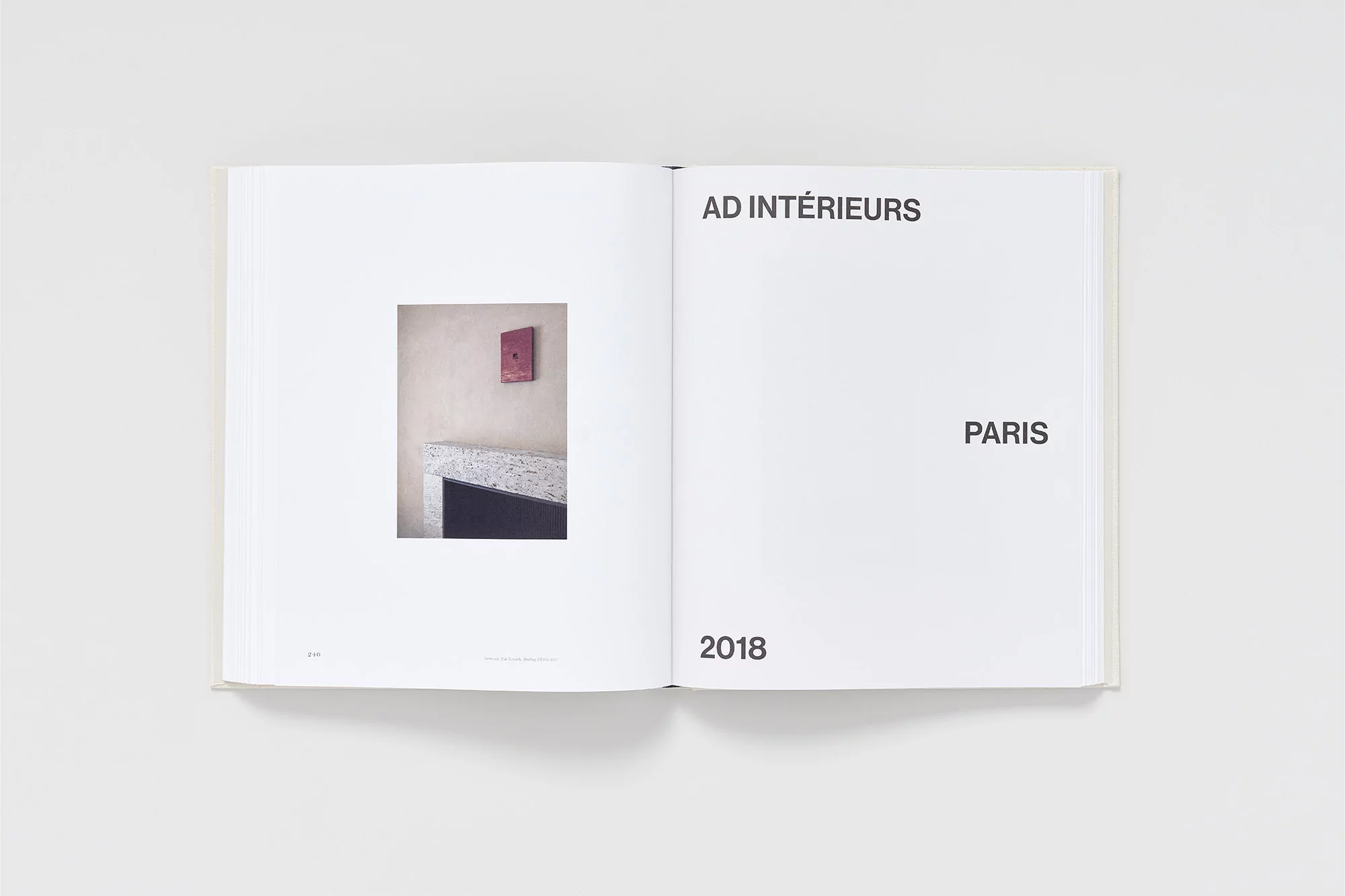 Open book displaying a photograph of a red painting above a fireplace, showcasing interior design elements.