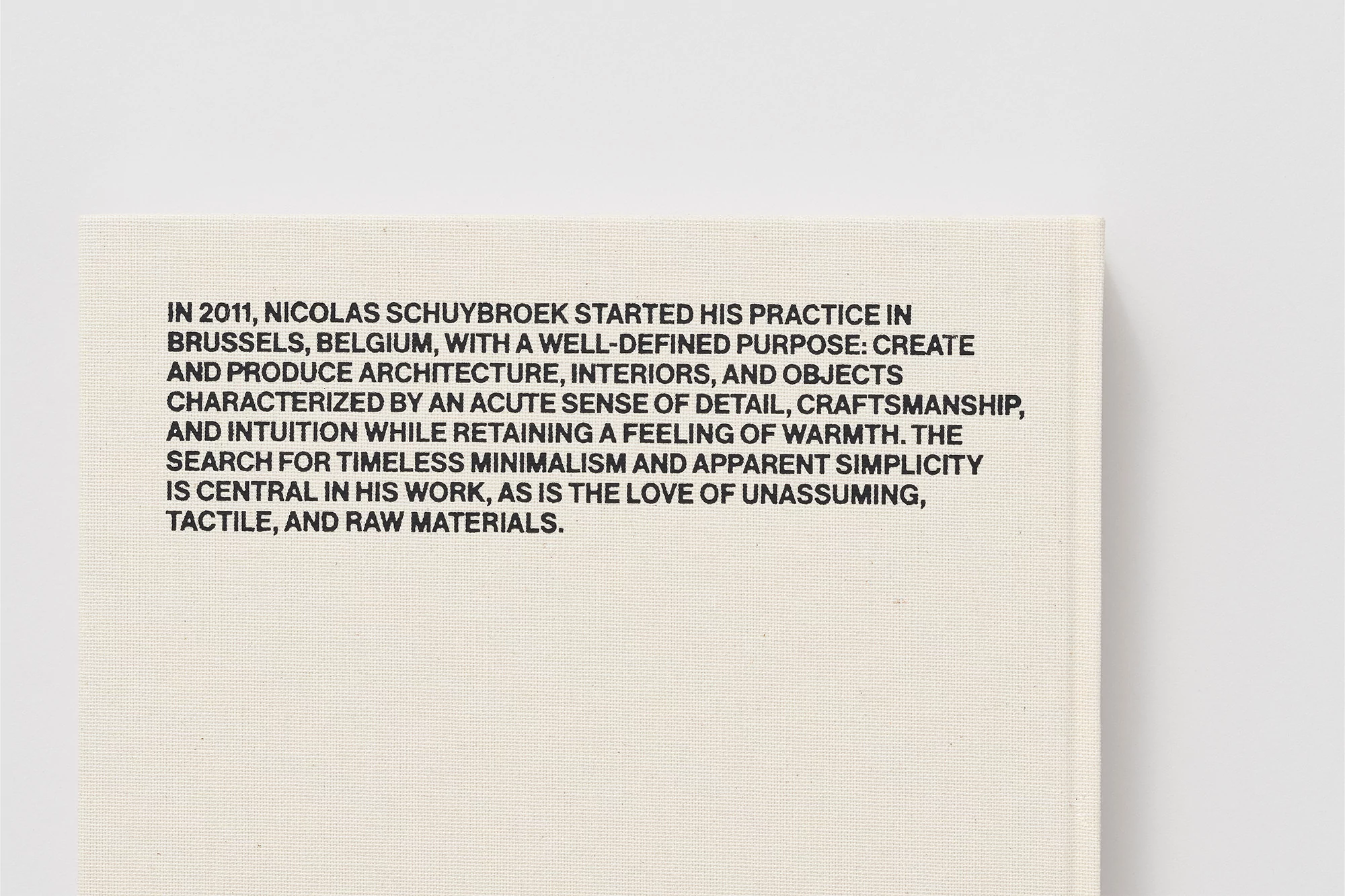 Close-up of a book cover with descriptive black text about the architecture practice of Nicolas Schuybroek on a textured beige background.