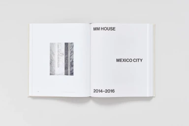 An open monograph book laying flat on a neutral surface, displaying typographic layout and architectural photography.