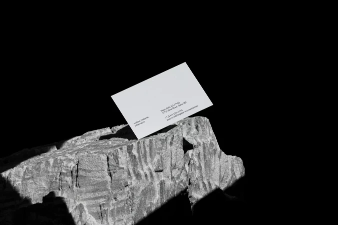 Elevated view of a business card atop a textured rock against a stark black backdrop, featuring company contact details and logo.