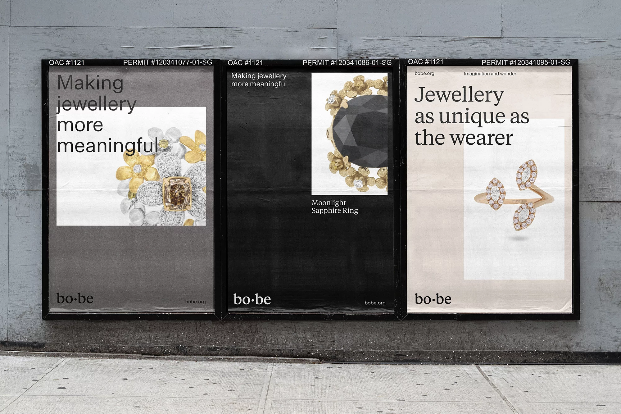 Three jewellery advertisements on a grey concrete wall feature rings. The left poster has flower motif, the center ring is sapphire, and right is angular.