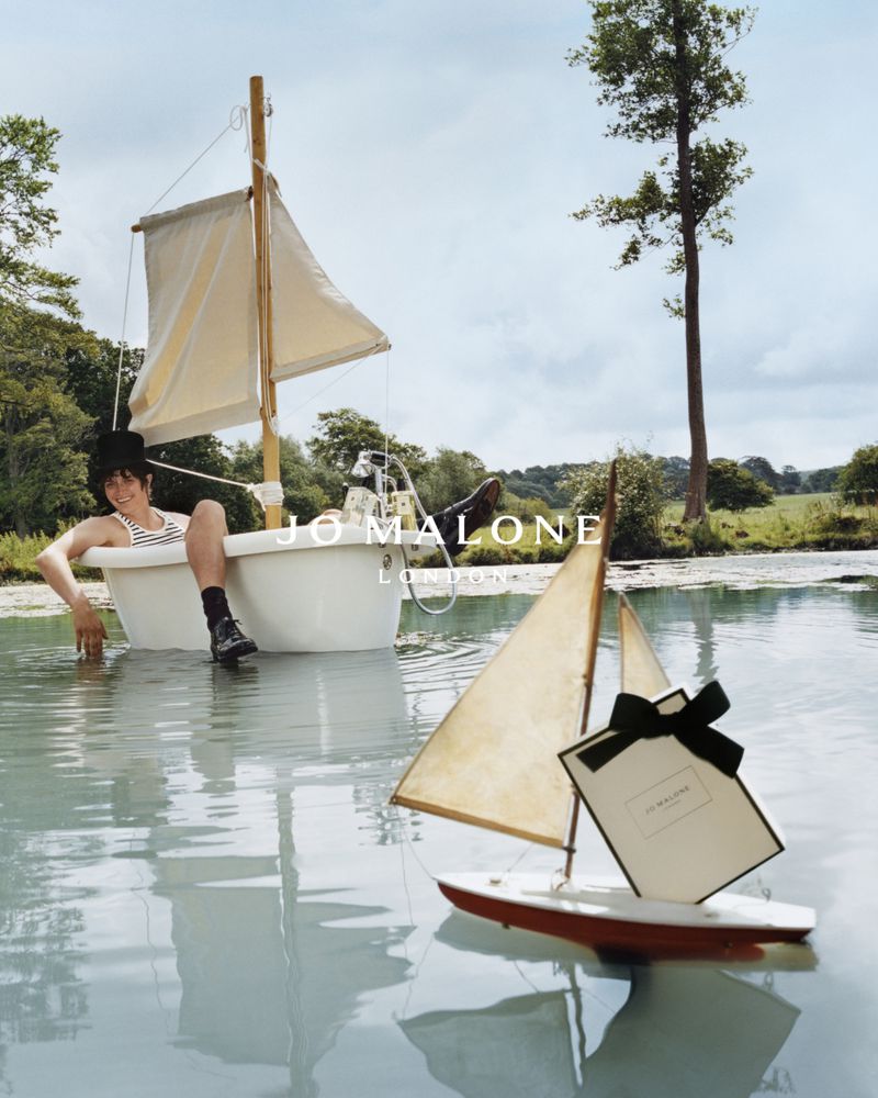 Child reclines in bathtub sailboat on a lake, Jo Malone gift, capturing whimsical outdoor beauty and youthful nautical themes.