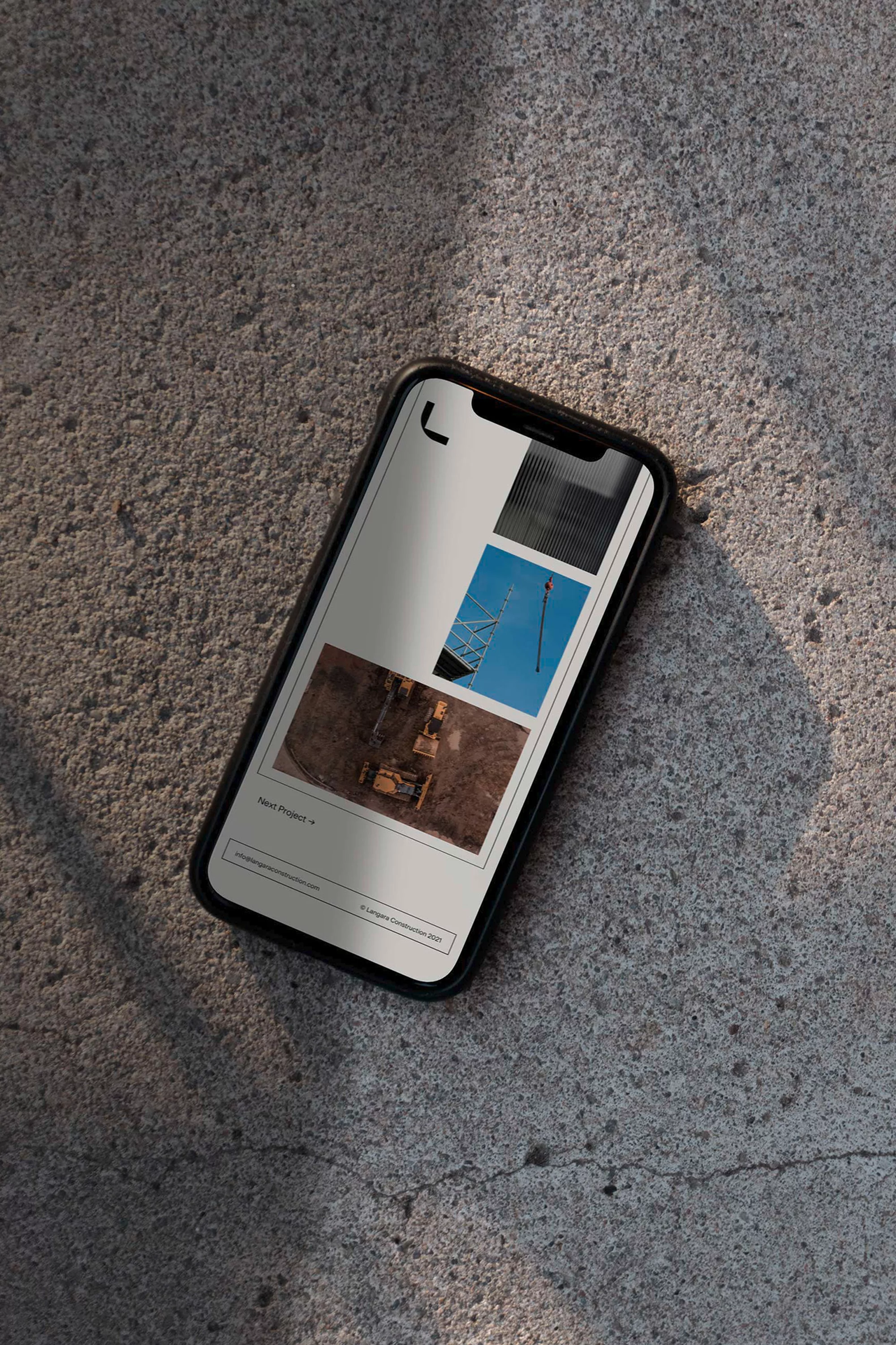 Smartphone displays construction site images, angled on concrete. Mobile phone shows architecture or engineering project, shadowed on stone.