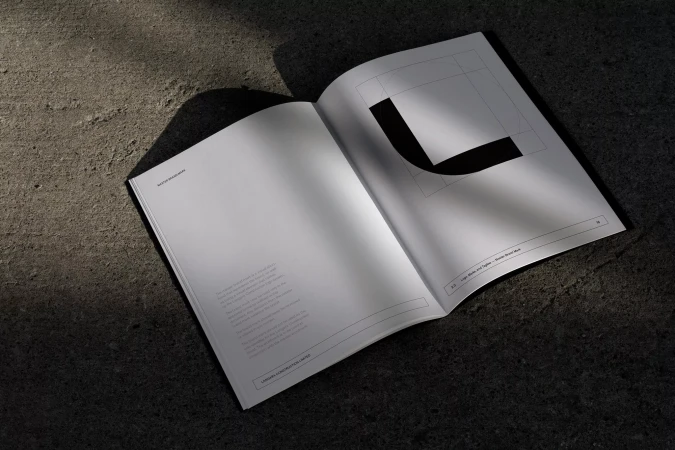 An open brand identity guidelines book displaying typography and geometric logo marks on a dark textured concrete surface.