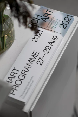 Promotional materials on a white table featuring art fair dates and program details, showcasing art and design events in August 2021.