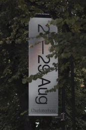 Vertical banner for CHART with dates 27-29 Aug and Charlottenborg text hanging between green tree branches outdoors.