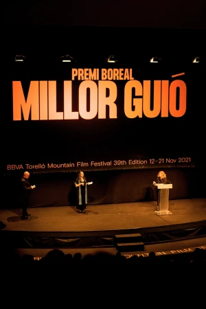 Panel discussion at the Torelló Mountain Film Festival features three speakers on stage under event signage in a darkened auditorium.