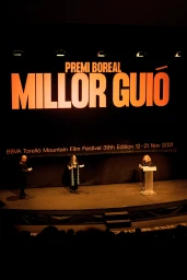 Stage presentation at the Torelló Mountain Film Festival with three people standing under a large banner reading PREMI BOREAL MILLOR GUIÓ.