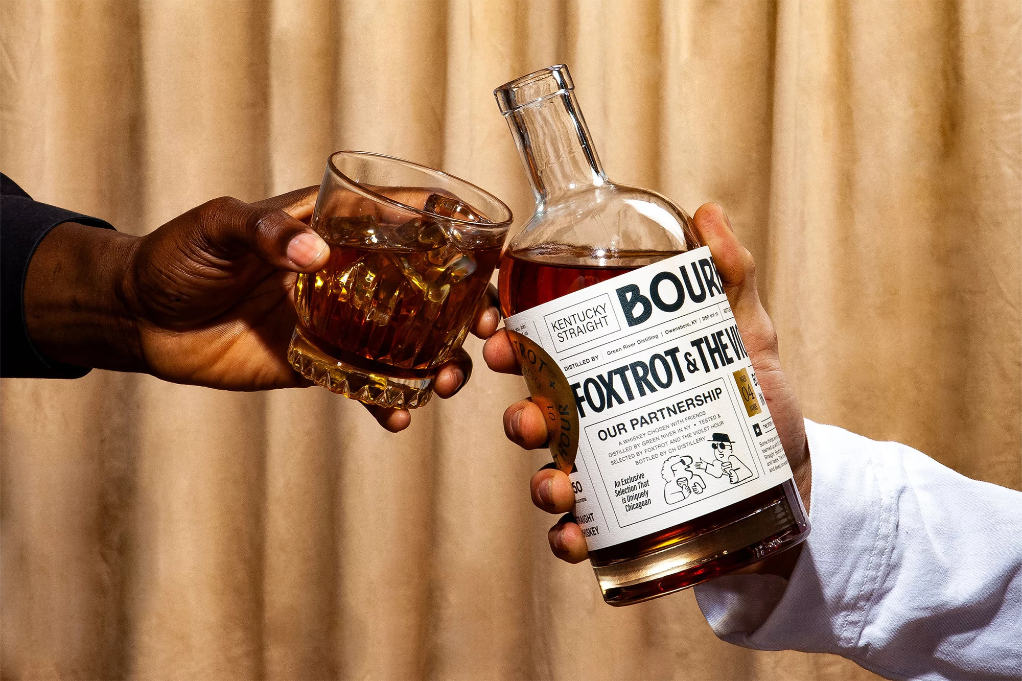 Two hands holding an uncut glass of whisky with ice cubes and a whiskey bottle against a tan curtain in a brightly lit room.