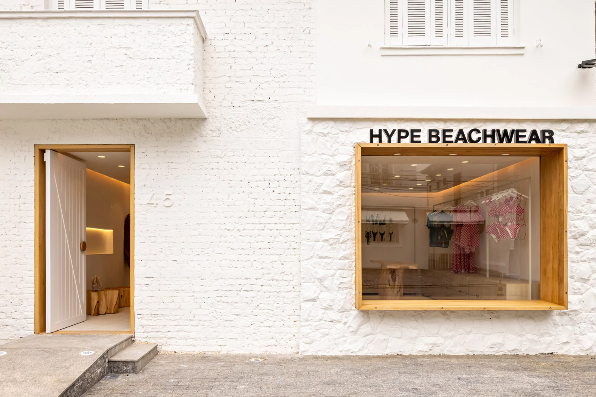 The exterior of Hype Beachwear featuring a window display and open doorway on a bright white brick building in daytime.