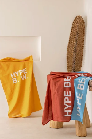 Folded colorful beach towels featuring printed brand text displayed in a minimalist neutral interior setting.