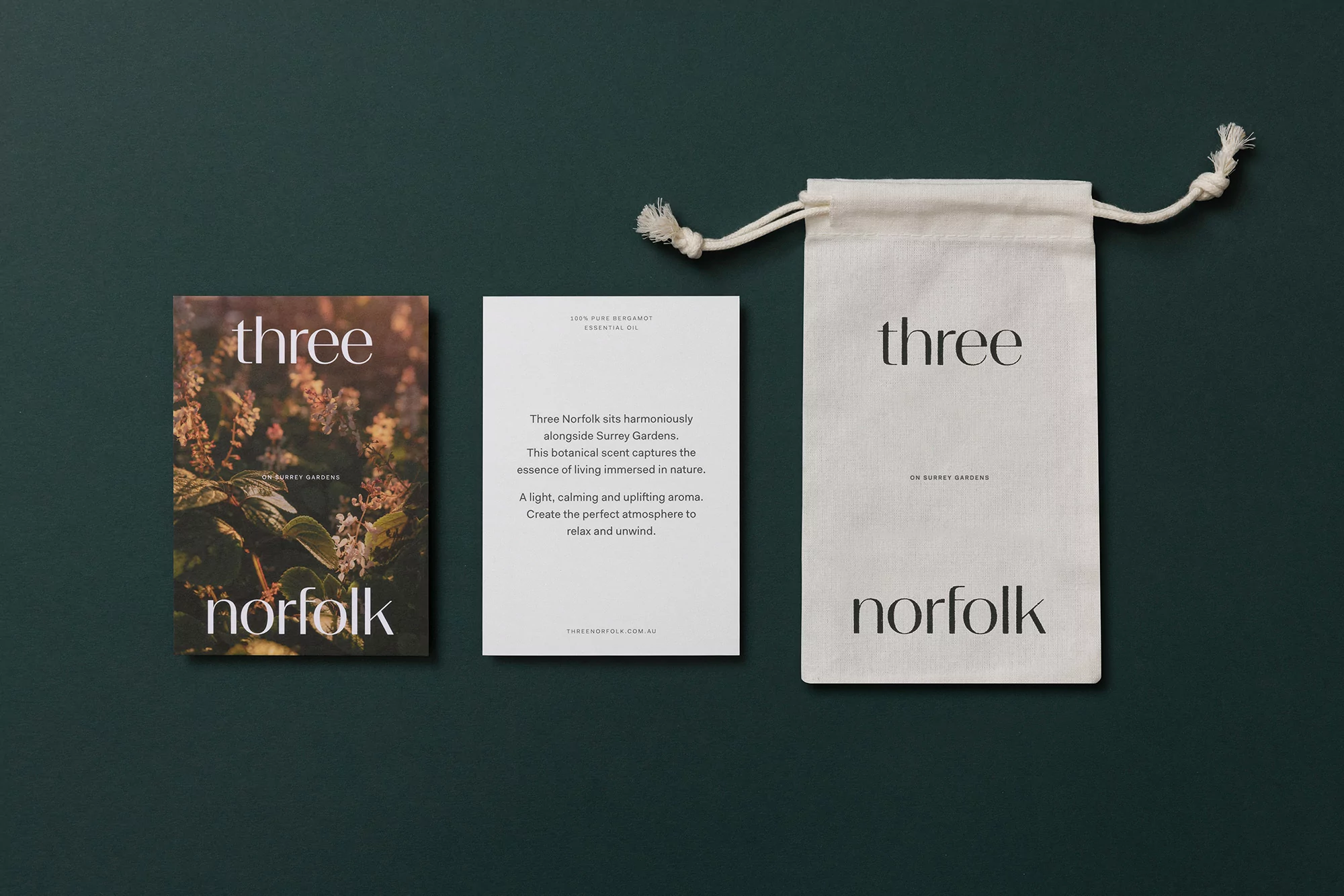 Close-up of a fragrance product set: a botanical print book, an information card, and a small cotton drawstring bag, all with branding.