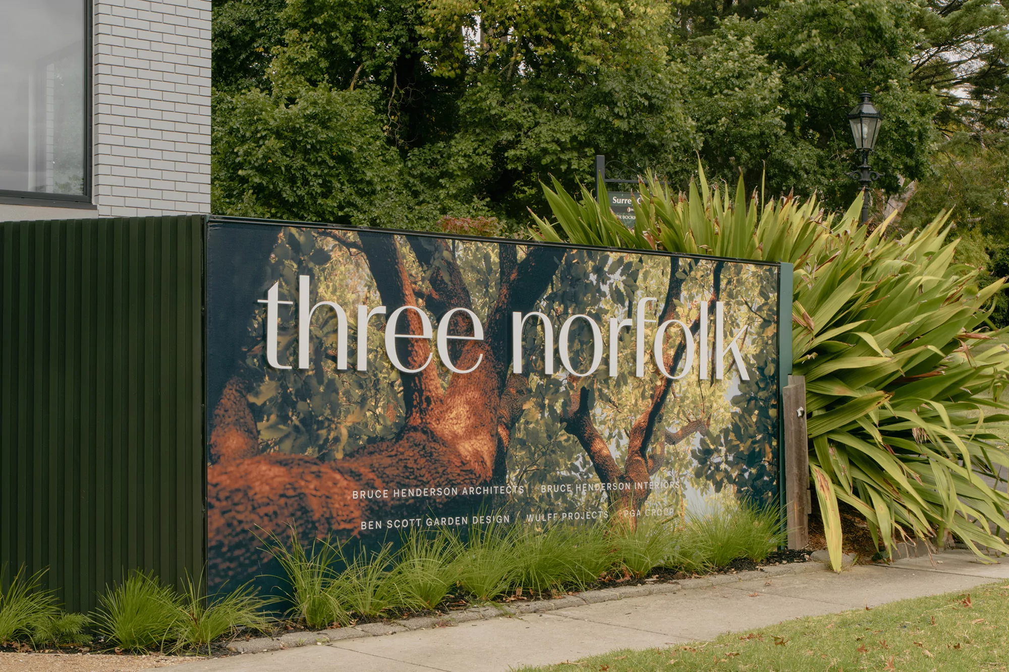 Signage with 'three norfolk' text, trees, and shrubbery. The design features the names of associated architects and designers.