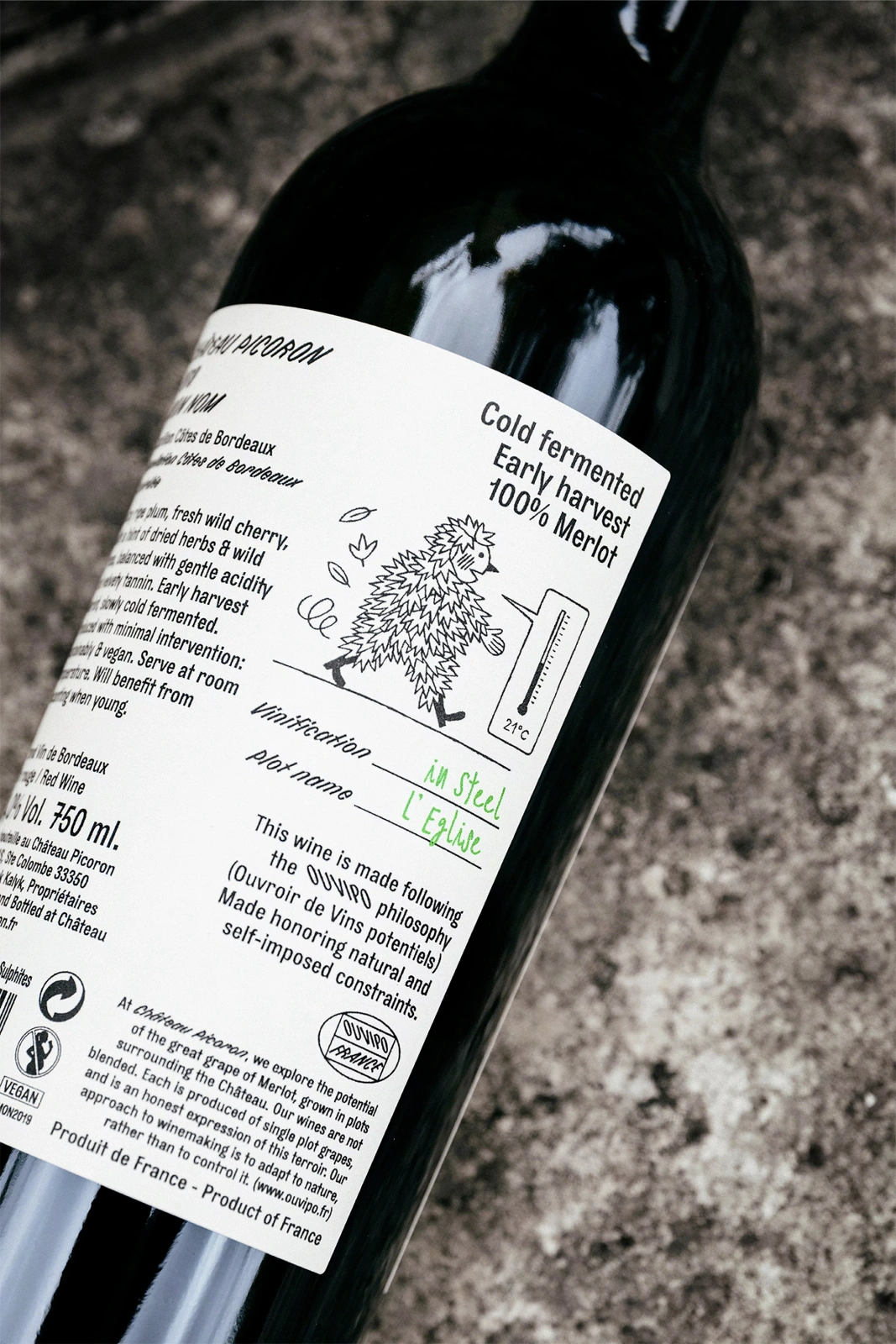 Close-up of a wine bottle featuring a detailed white paper label with illustrated character and text against a textured stone surface.