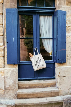 Tote bag with text hanging on a blue door handle of a stone building with blue shutters