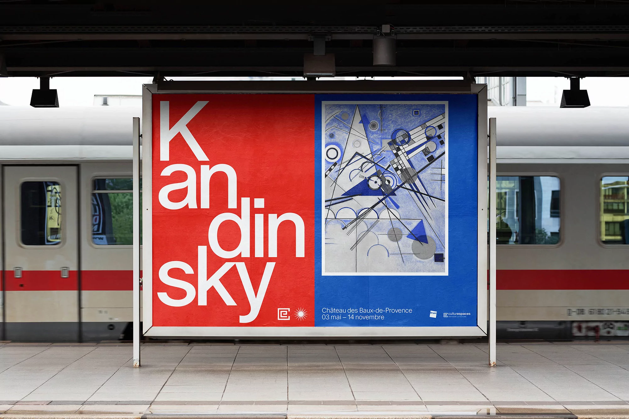 Large outdoor advertisement with Kandinsky artwork and text, displayed on a train platform with a passenger train in the background.