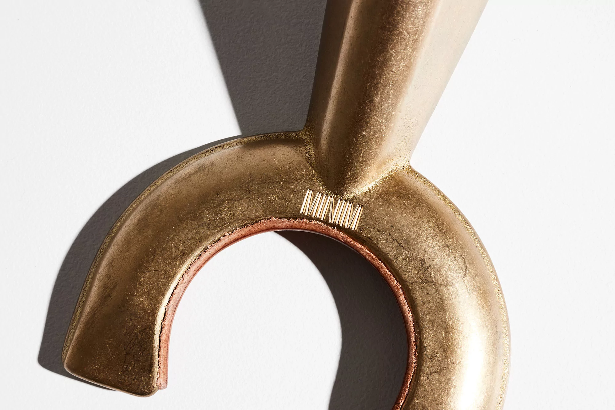 Close-up shot of a bronze, crescent-shaped bottle opener against a clean white backdrop with subtle shadows, highlighting its form and texture.