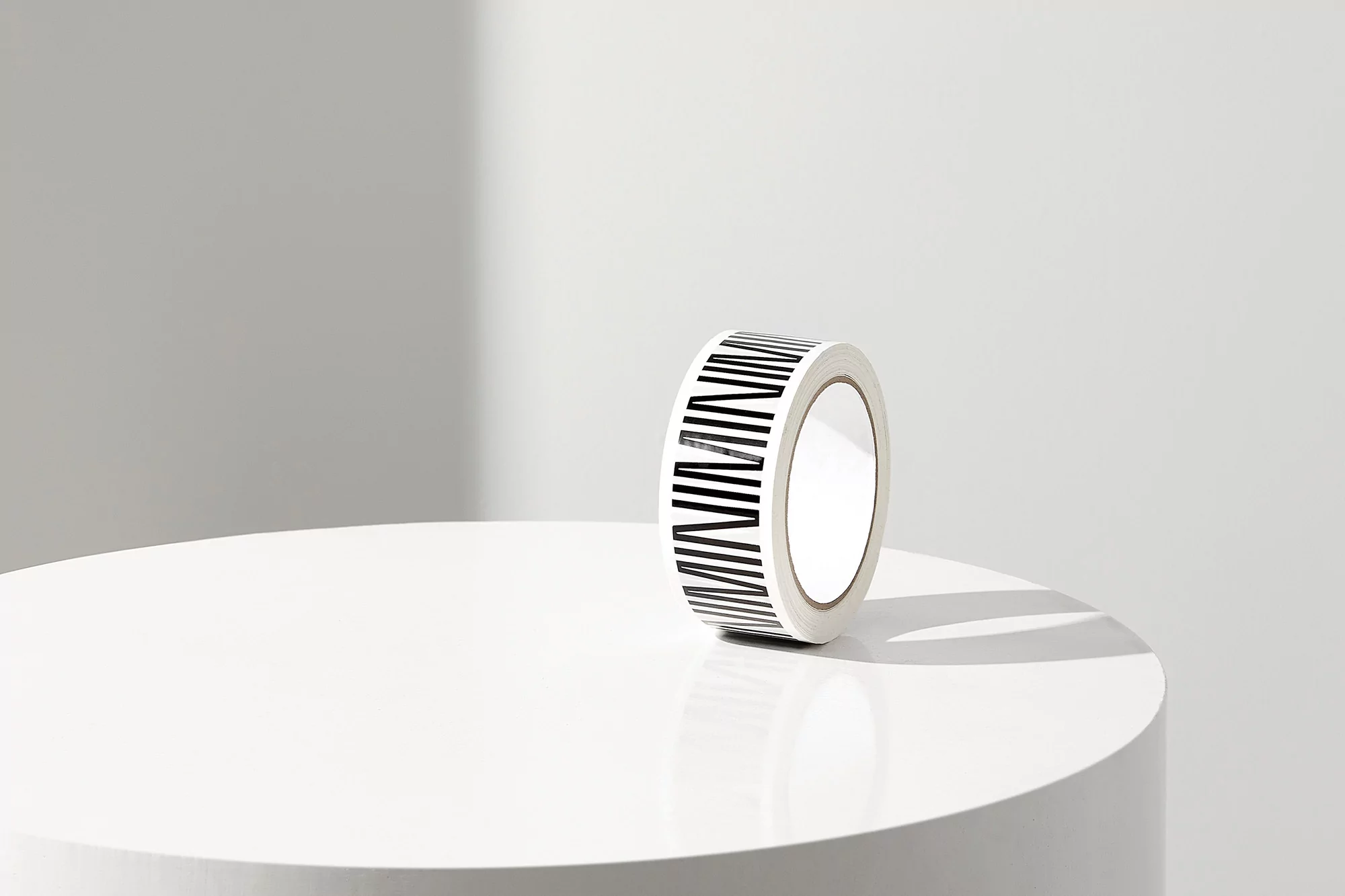 Close-up of a roll of white masking tape with black stripes sitting on a white cylindrical table in a bright, minimalist interior.