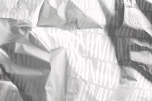 Crumpled white paper surface featuring repeating typographic branding patterns under soft directional lighting.