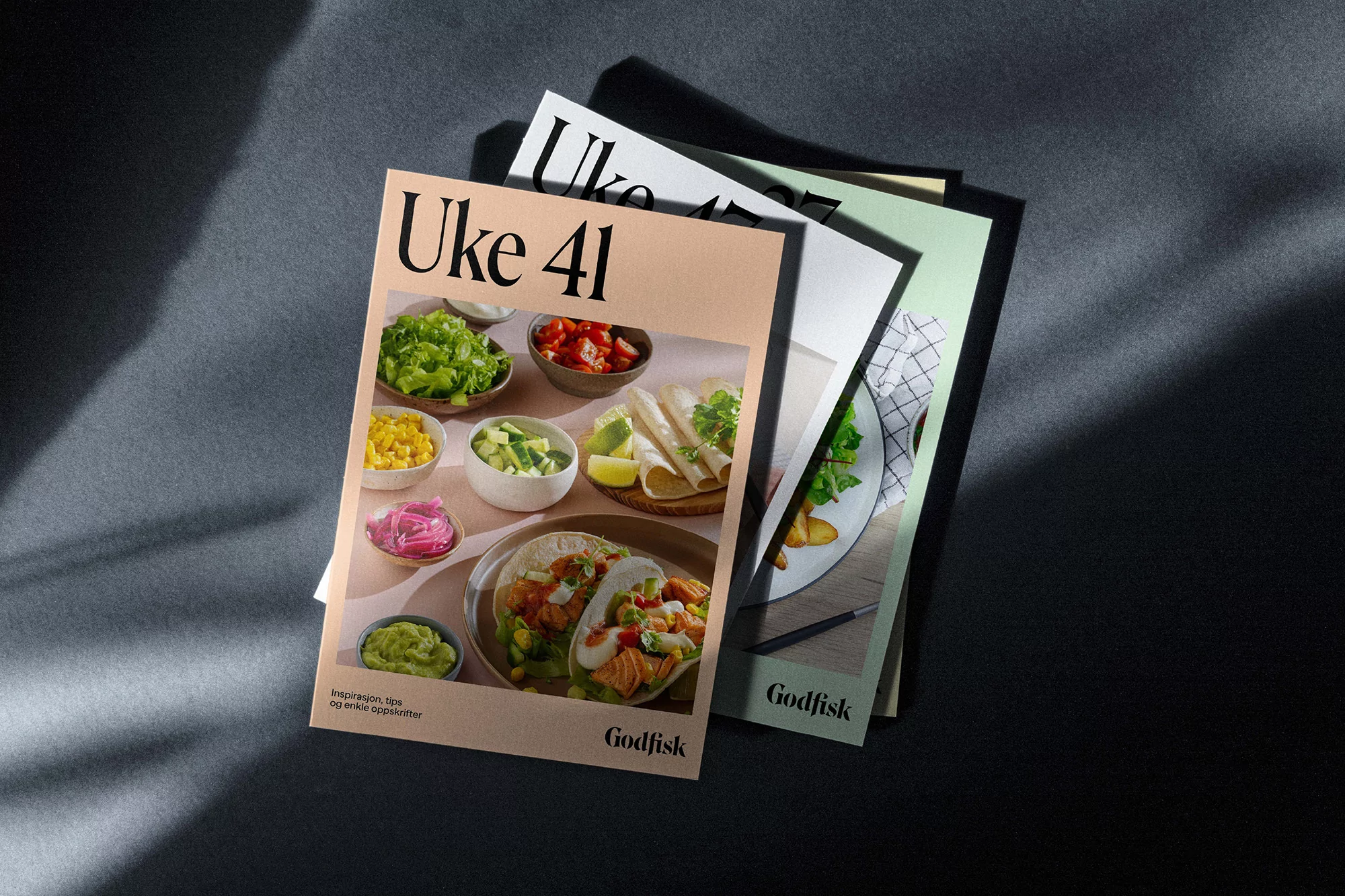 Close-up of food magazine covers with taco and salad images on a grey surface with light and shadow creating contrast.
