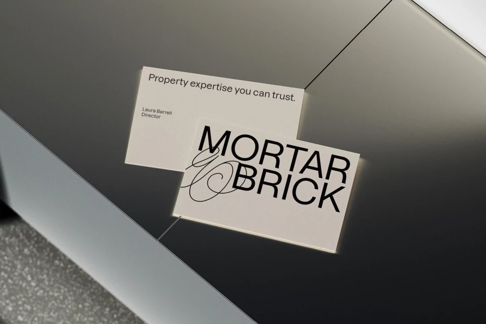 Two business cards on a gray surface: one reads, 'Property expertise you can trust,' the other 'Mortar & Brick' in black text.