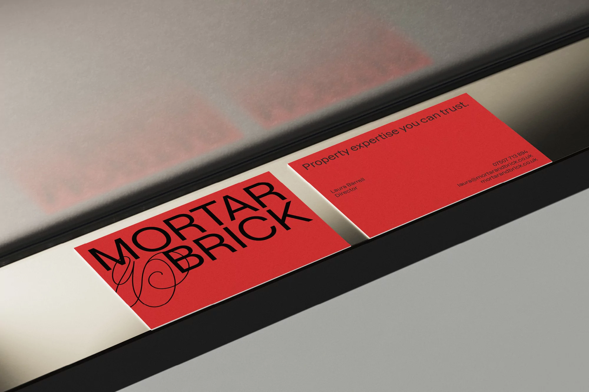 Close-up of two red business cards with black text, one displaying the company name and logo, the other contact information.