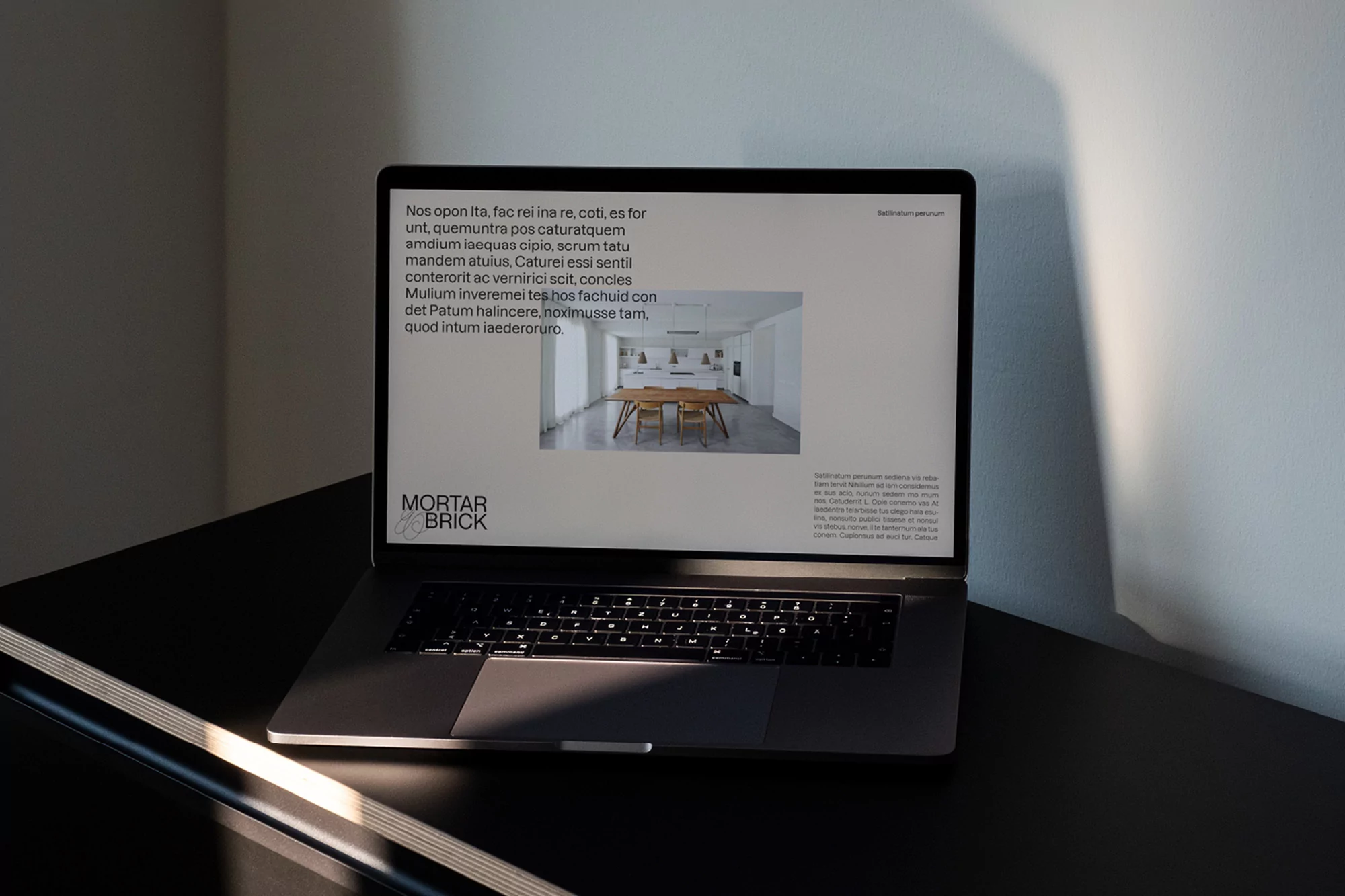 Laptop on a black desk displaying a website for Mortar Brick, featuring an interior design photo and text in a softly lit room.