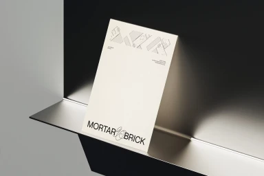 Branded letterhead stationery mockup featuring the Mortar and Brick logo resting against a dark minimalist metallic shelf