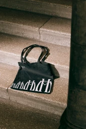 Black tote bag with white typographic graphics resting on weathered granite stone steps
