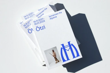 Stack of white printed cards with blue typography and an image of Ötzi the Iceman resting on a white surface.