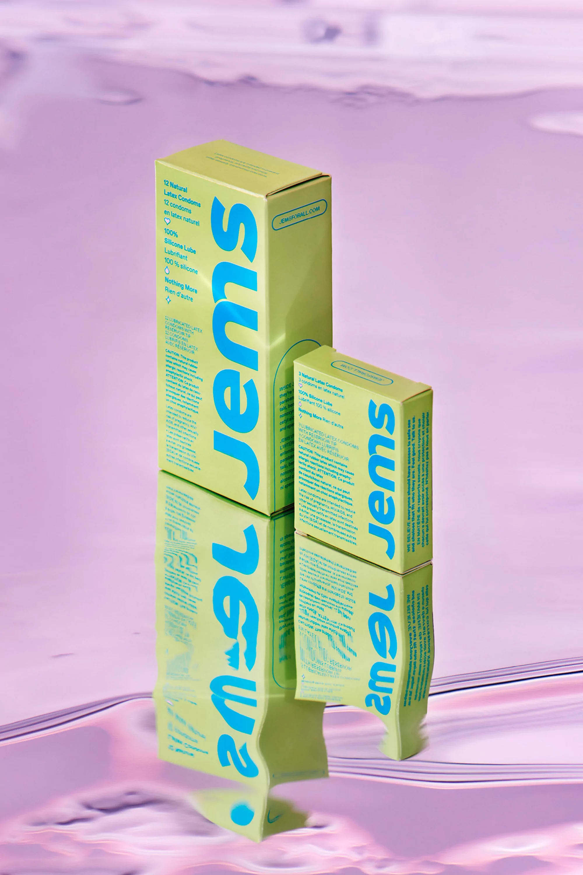Two Jems condom boxes in a studio setting. One tall, one short. Text on the boxes in blue. Reflective surface with a blurry background.