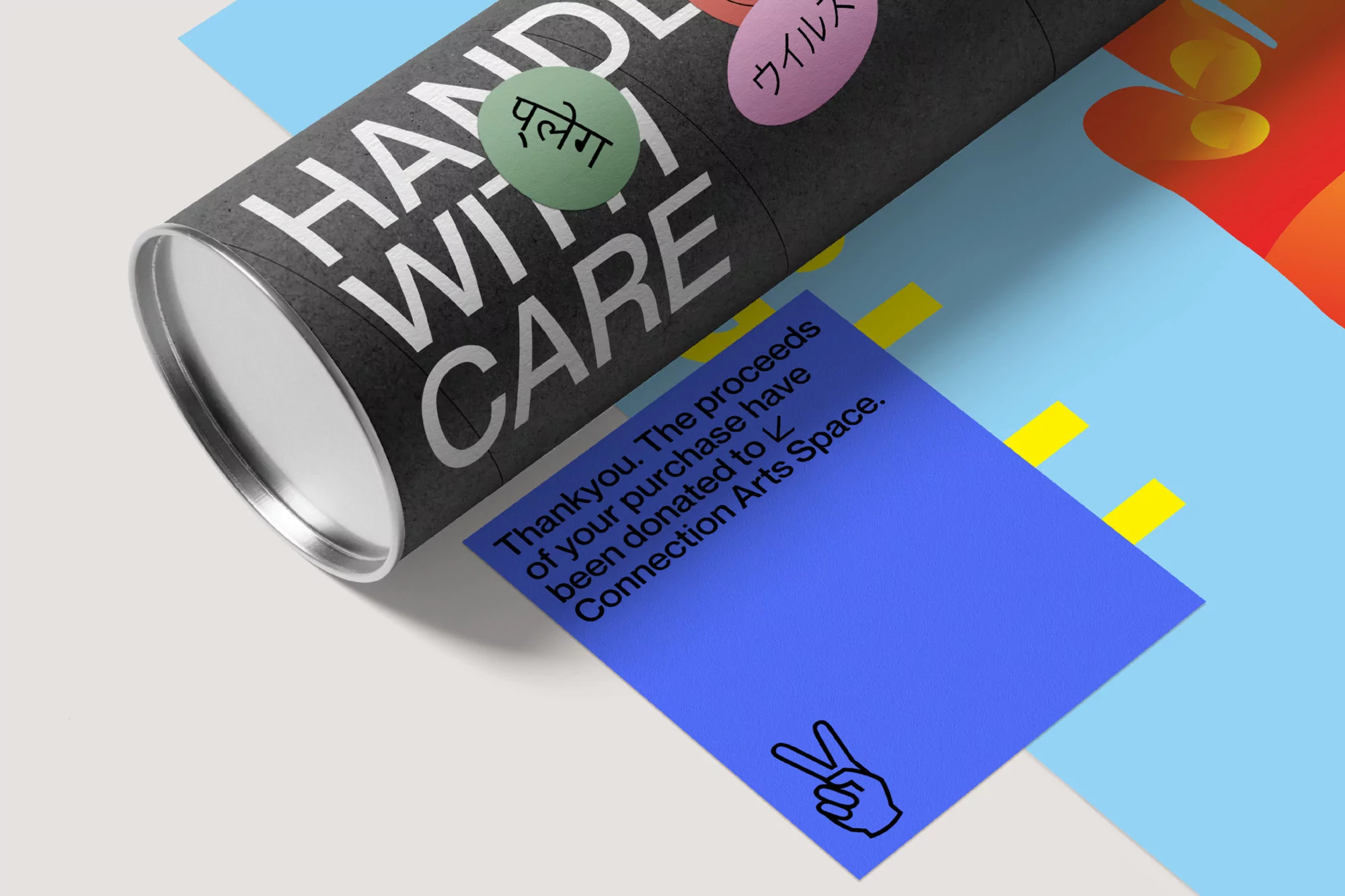 Angled studio shot of a black cylindrical tube with 'Handle With Care' text and stickers, alongside a blue thank you note.