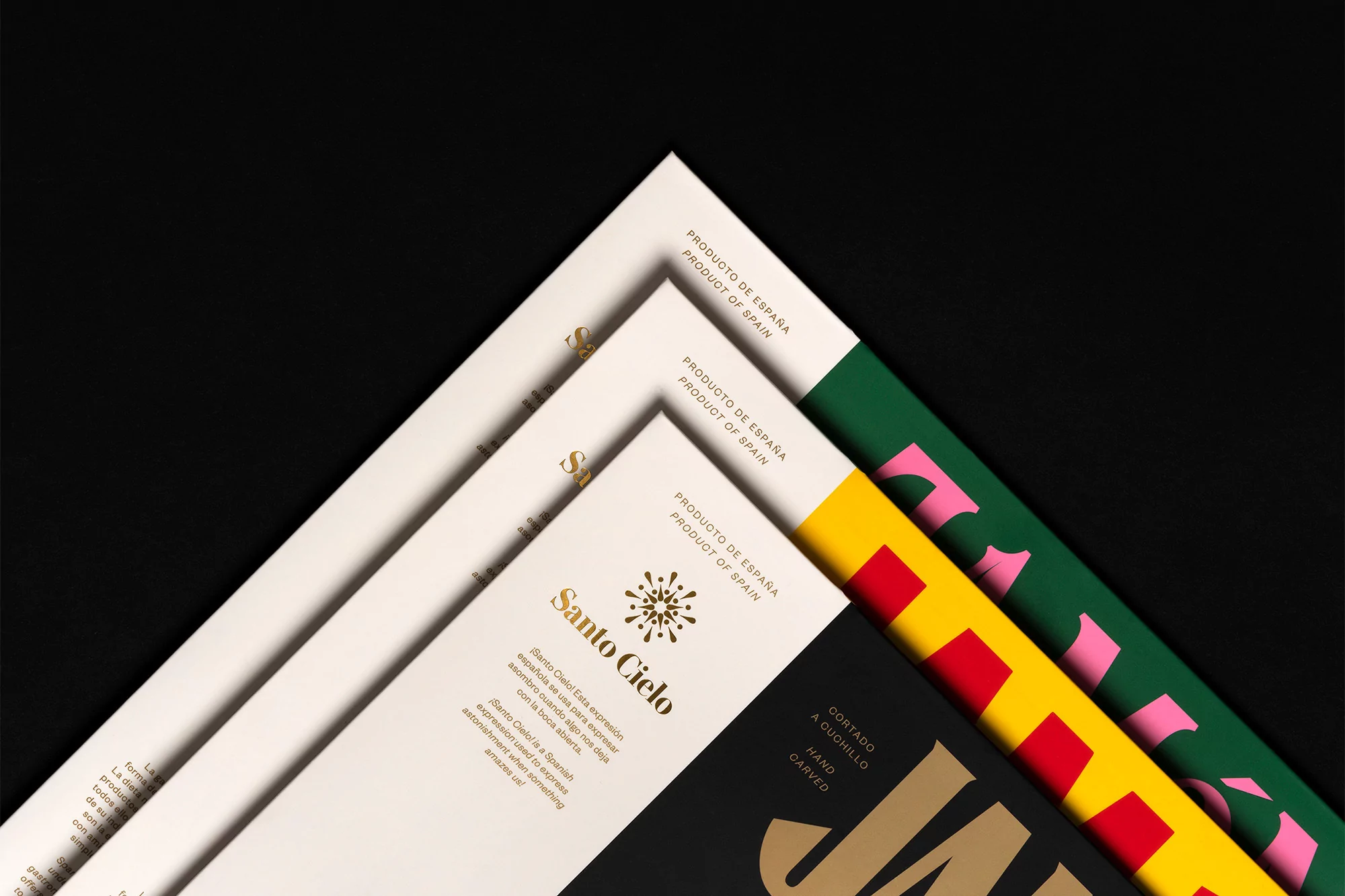 Overhead shot of stacked product packaging with gold lettering on black and white backgrounds against a dark background.