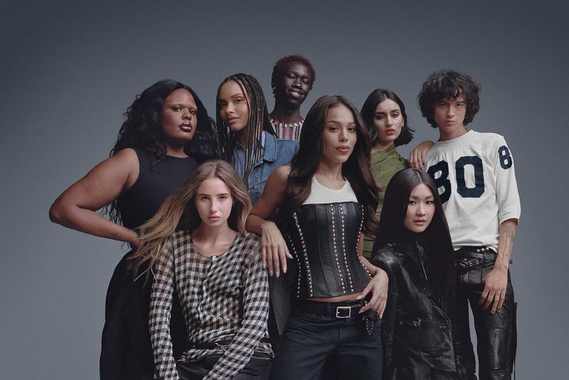 Diverse group of eight models posing together in a studio. The subjects wear a mix of stylish clothing, including leather and denim jackets.
