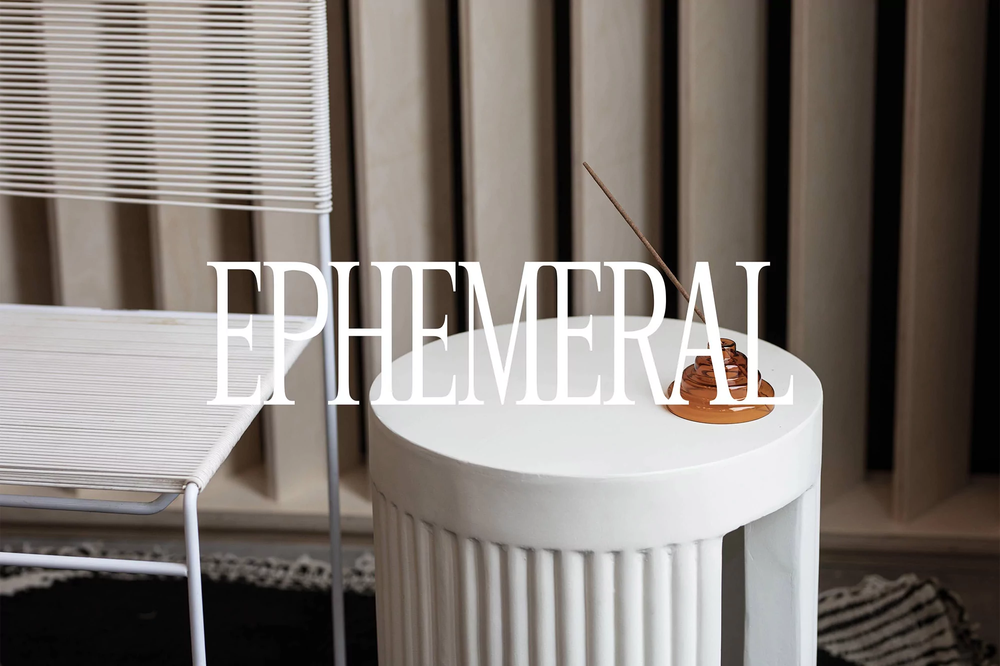 Minimalist interior featuring a white woven chair, round side table, and an incense burner with a lit incense stick creating a calming atmosphere.