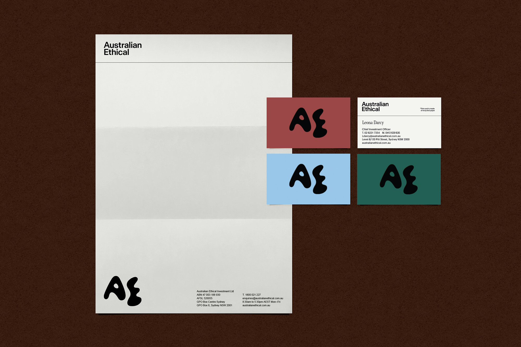 Letterhead and business cards featuring a black logo on white paper and colored cards, set against a brown textured background.