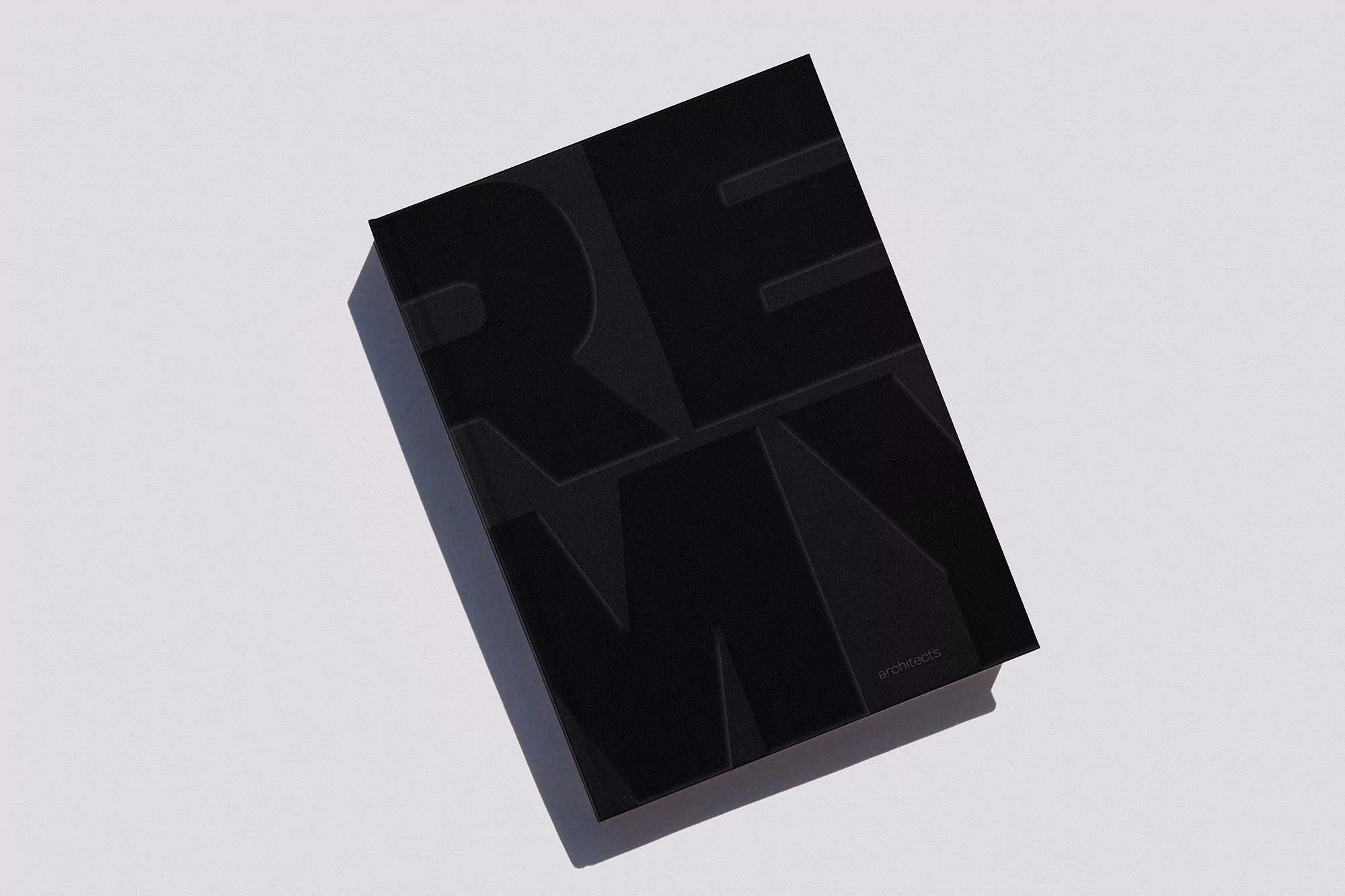 Black rectangular book with embossed, sans-serif typography, illuminated by bright, neutral lighting on a plain light grey surface.