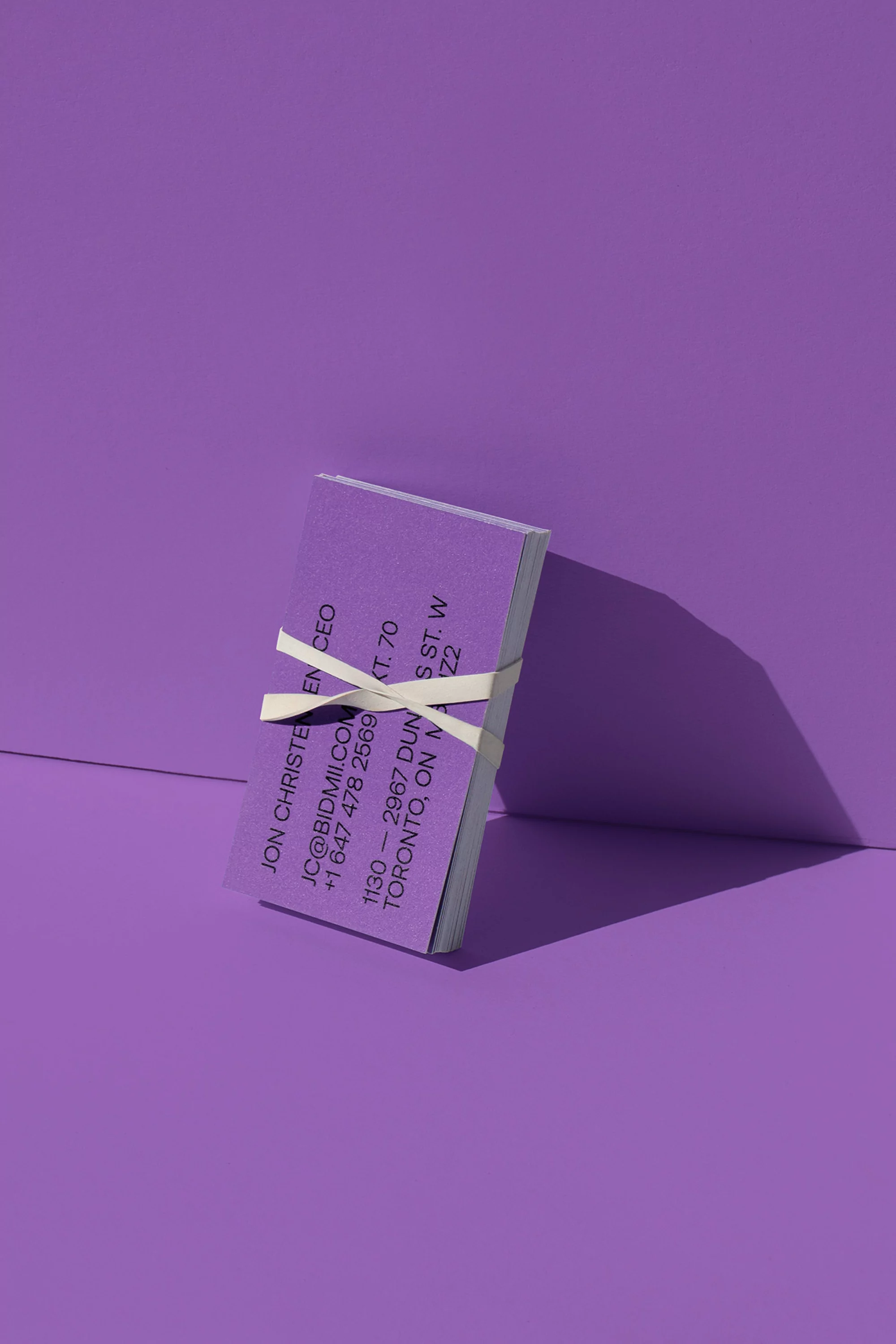 Stack of purple business cards secured with white rubber band against matching background. Shadow adds depth. Clean, minimalist design.