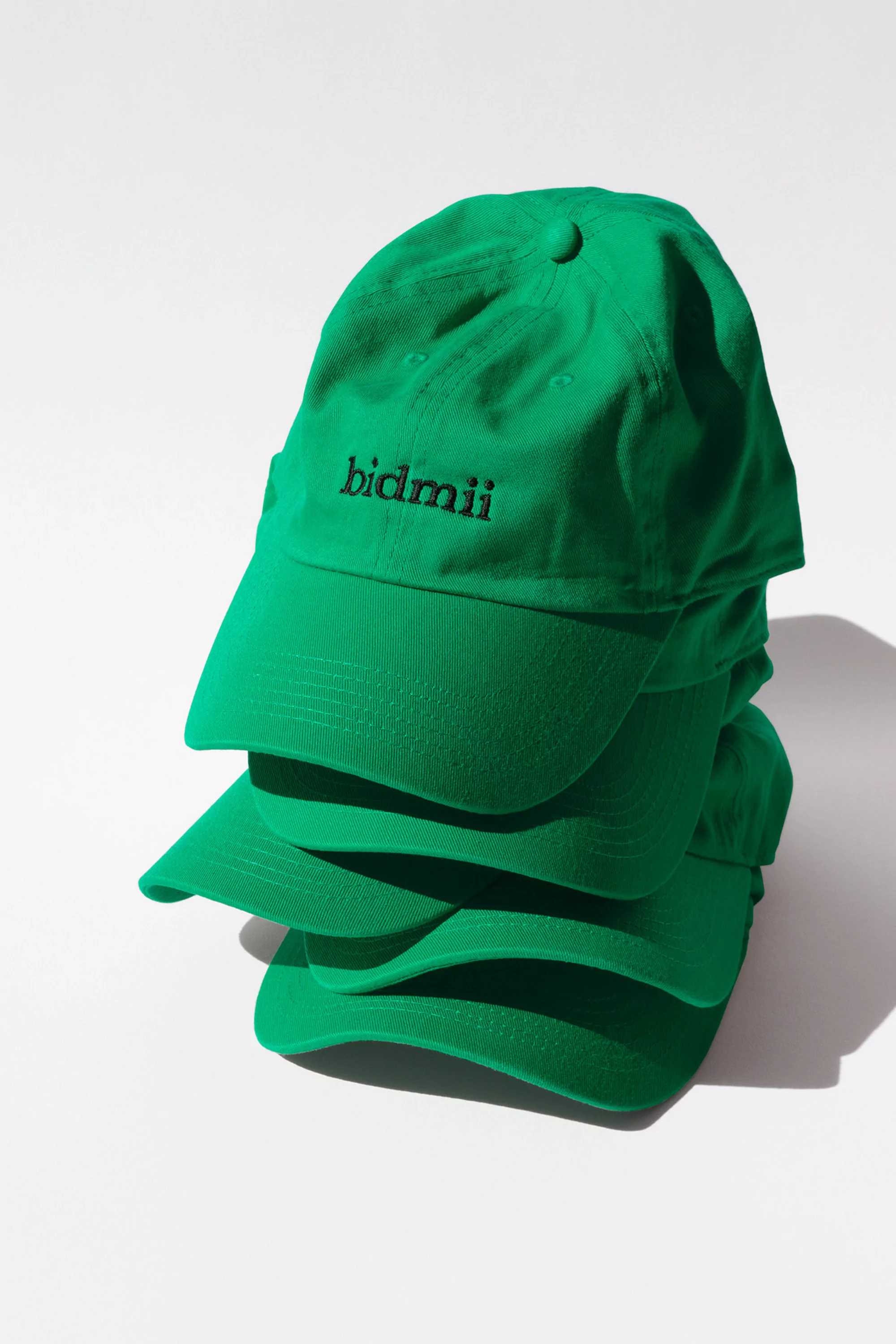 Stack of bright green baseball caps with 'bidmii' logo against a white backdrop, perfect for fashion, apparel, and promotional material visuals.