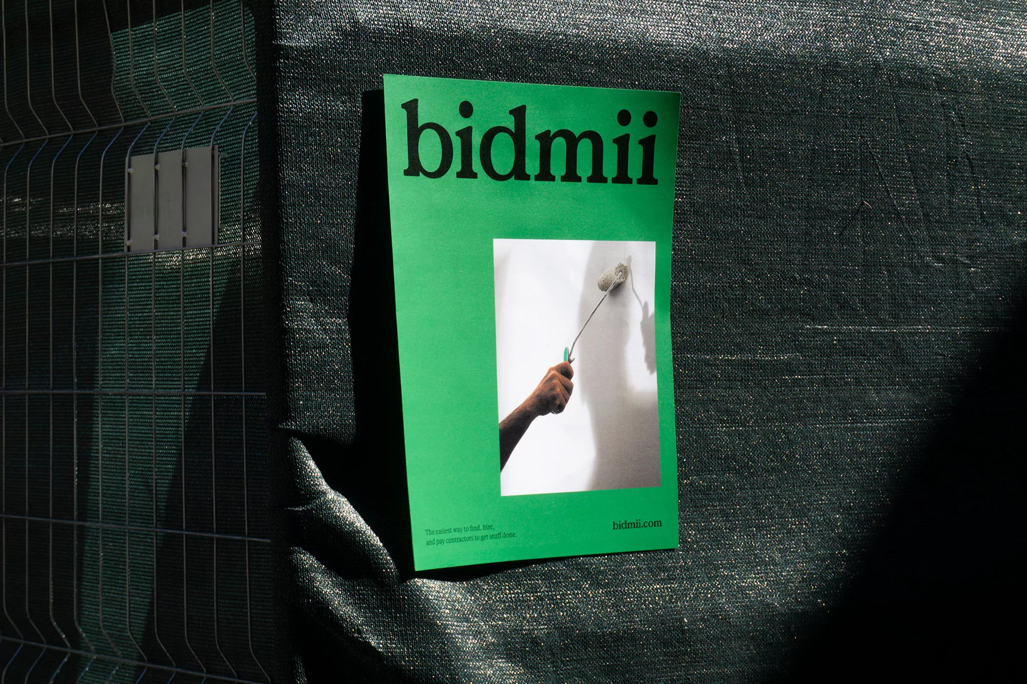 Promotional image featuring a green bidmii flyer attached to a chain-link fence, showcasing a hand painting a wall with a roller.