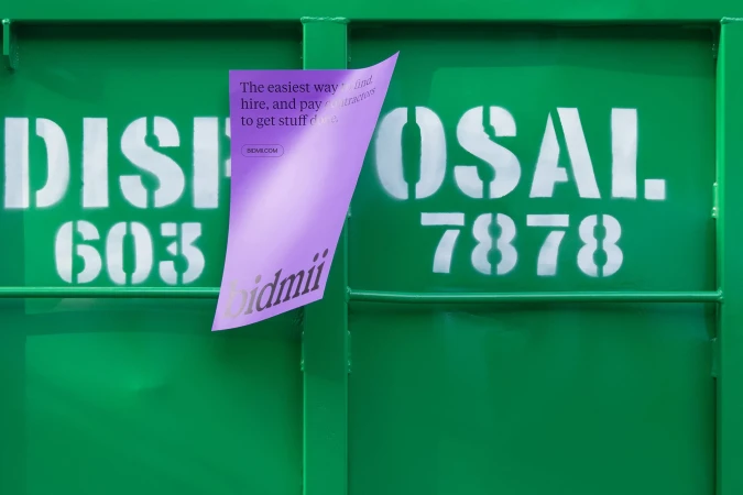 Promotional image featuring an advertisement for Bidmii pasted on a green metal industrial door with white stenciled text on it.