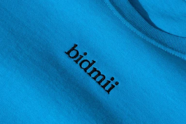 Close-up of a blue t-shirt with embroidered black text reading bidmii on the chest.