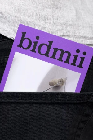 Close-up of a purple card with Bidmii branding tucked inside the dark denim back pocket of black jeans.